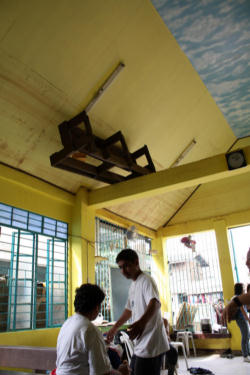 'Pew, That Was Close': Flood survivors receive aid at a chapel in Marikina, Philippines. When tropical storm Ketsana hit the island, massive flooding drove thousands from their homes. Father Javier Mexicano, shown here standing, was caught in his small parish house during the storm. He and another priest broke through the roof, waited there for the waters to settle, and eventually swam to safety.
<br>
<br>A pew is lodged in the rafters of the chapel, where it floated during the flood.The chapel's name? Our Lady of Perpetual Help.
<br>
<br>Photo: Laura Sheahen/Catholic Relief Services
<br>
<br> Image of 'Pew, That Was Close': Flood survivors receive aid at a chapel in Marikina, Philippines. When tropical storm Ketsana hit the island, massive flooding drove thousands from their homes. Father Javier Mexicano, shown here standing, was caught in his small parish house during the storm. He and another priest broke through the roof, waited there for the waters to settle, and eventually swam to safety.
<br>
<br>A pew is lodged in the rafters of the chapel, where it floated during the flood.The chapel's name? Our Lady of Perpetual Help.
<br>
<br>Photo: Laura Sheahen/Catholic Relief Services
<br>
<br>