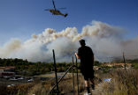 An area resident looks on as helicopters are used to fight the flames. Image of An area resident looks on as helicopters are used to fight the flames.