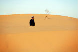 A Chinese man gazes over the sand of an advancing dune. Image of A Chinese man gazes over the sand of an advancing dune.