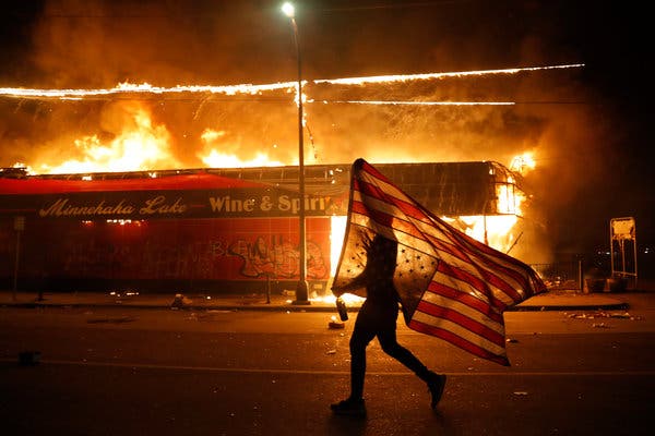 A protester carries the American flag upside down, a symbol of distress as Minneapolis burns. Image of A protester carries the American flag upside down, a symbol of distress as Minneapolis burns.