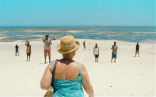 A still from the film depicting a woman shopping for a male prostitute on the beach. Image of A still from the film depicting a woman shopping for a male prostitute on the beach.