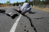 A road worker examines damage done by a quake in California. Image of A road worker examines damage done by a quake in California.