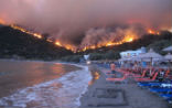 A man takes refuge on a beach in Greece as fires ravage the country. Image of A man takes refuge on a beach in Greece as fires ravage the country.