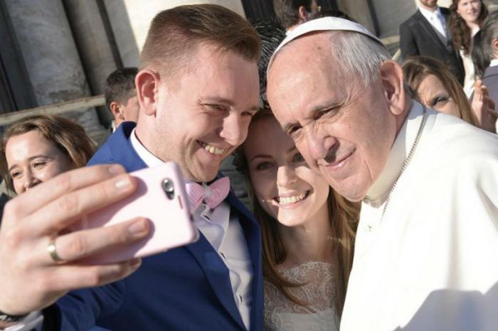 Pope Francis takes a selfie with a newly married couple. Pope Francis takes a selfie with a newly married couple.