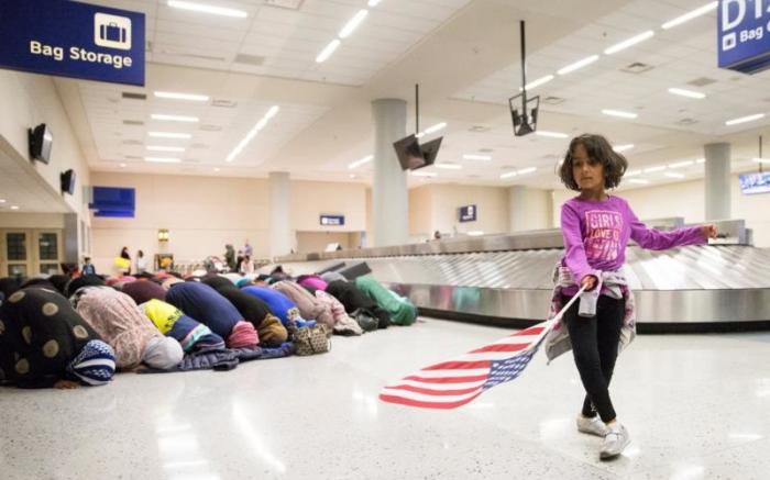 A young girl dances with an American flag at Dallas/Fort Worth International Airport as women pray during a protest against the travel ban.