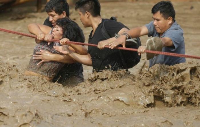 A group of people, stranded in flood waters, cling to a rope as they make their way to safety.