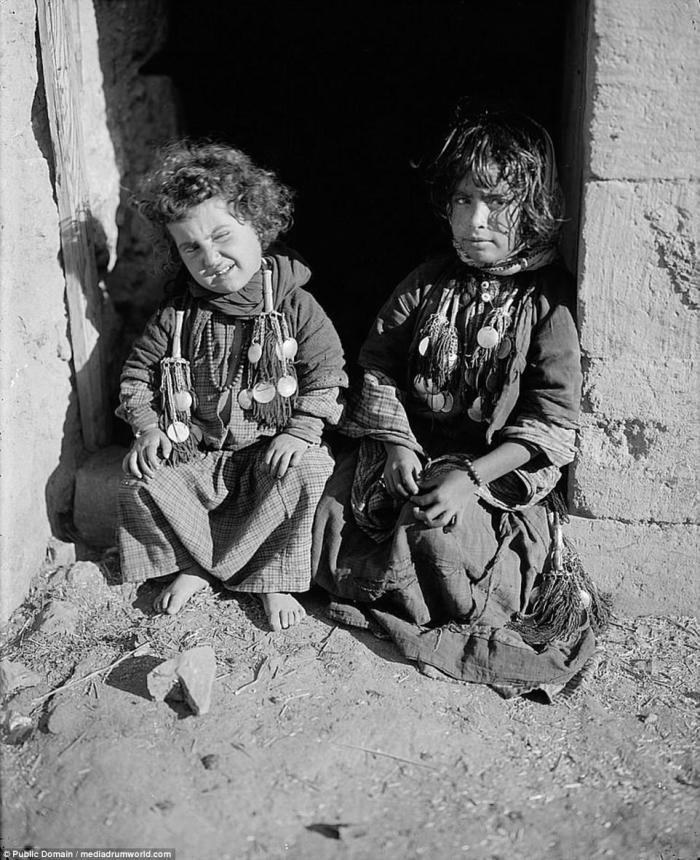 Bedouin children in traditional dress sit in a doorway for a picture. 