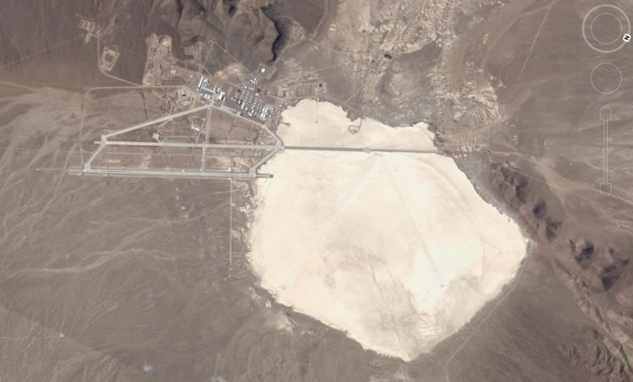 A satellite image of Groom Lake taken from Google. The curved runway is faintly visible as a line on the right side of the dry lakebed. 