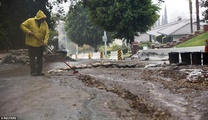 A resident sweeps water and debris as rain begins to fall in Glendora, California as a major Pacific A resident sweeps water and debris as rain begins to fall in Glendora, California as a major Pacific